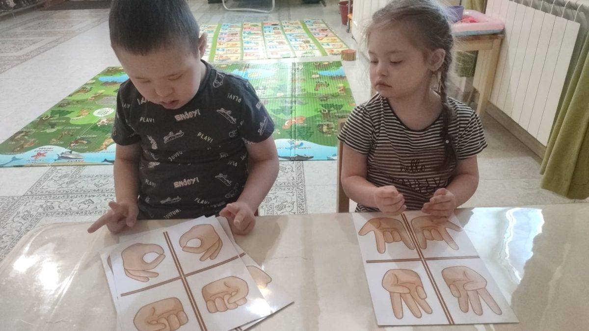 De jeunes enfants trisomiques sont aidés pour développer leur motricité fine.